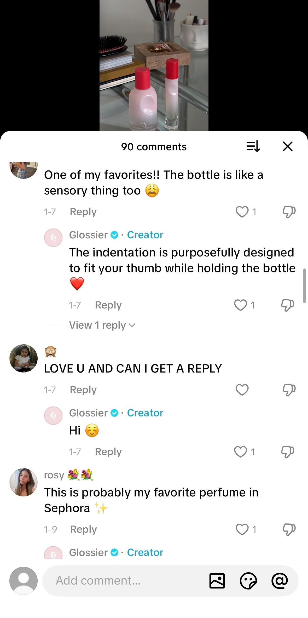 Close-up of two minimalist pink perfume bottles with red caps on a glass vanity table, shown within a social media comment thread.